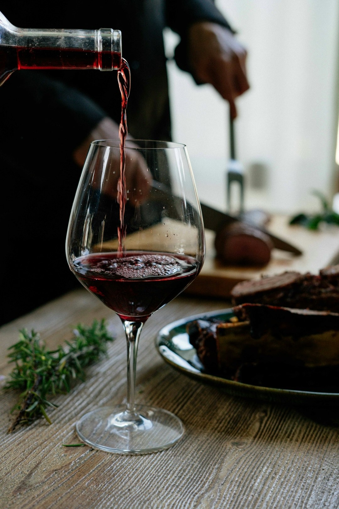 Glass of red wine on table with sprig of rosemary and steak
